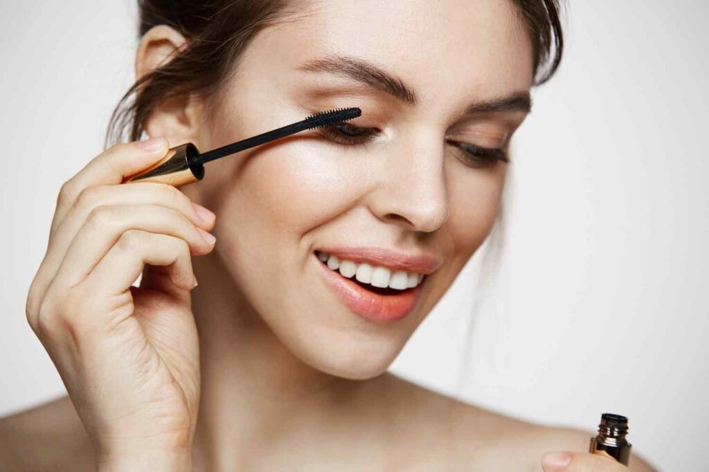 Woman holding mascara wand applying mascara to her eyelashes with a smile