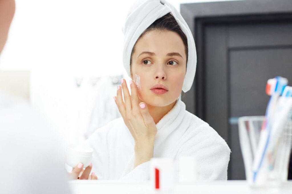 Woman applying face cream while looking in mirror