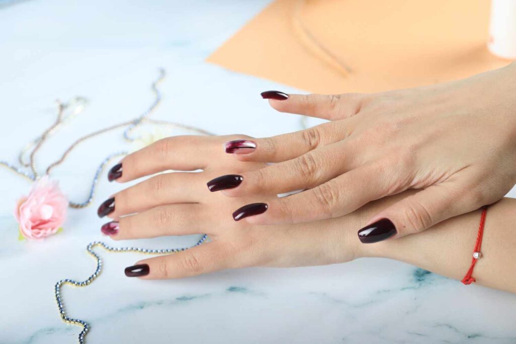 Close-up of hands with glossy burgundy fashion nails and subtle nail art on a light background with jewelry